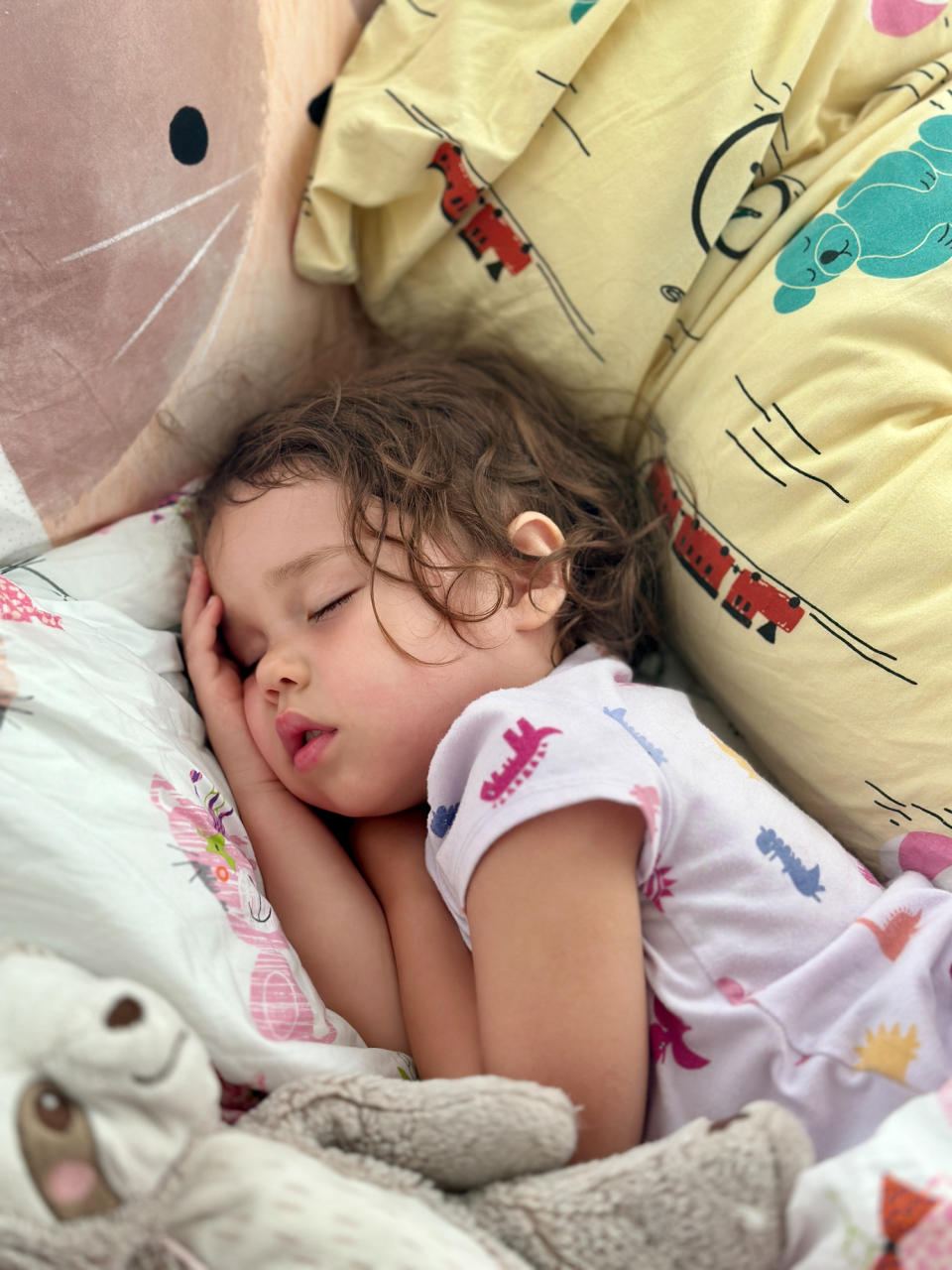 Child sleeping soundly in bed, surrounded by stuffed animals and cozy pillows with patterns of trains and animals