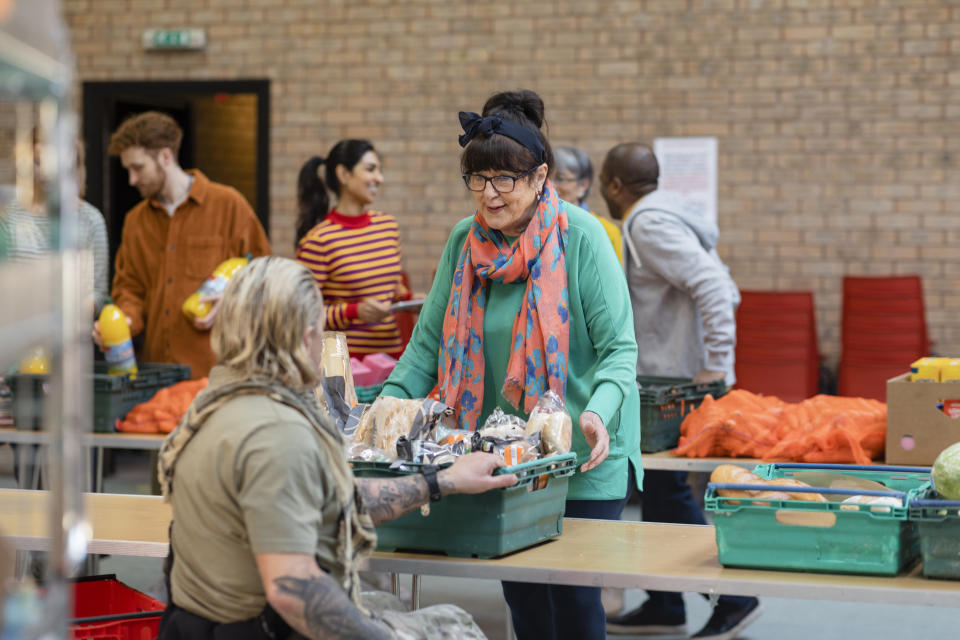 People volunteer and distribute food at a community center. A woman receives a box of food from another volunteer with tattoos on her arm