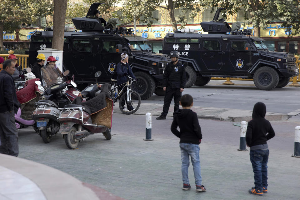 FILE - In this Nov. 5, 2017, file photo, residents watch a convoy of security personnel and armored vehicles in a show of force through central Kashgar in western China's Xinjiang region. China says on Monday, March 18, 2019 it has arrested nearly 13,000 people it describes as terrorists in the traditionally Islamic region of Xinjiang since 2014 and broken up hundreds of "terrorist gangs." The figures were included in a government report on the situation in the restive northwestern territory that seeks to respond to growing criticism over the internment of an estimated 1 million members of the Uighur and other predominantly Muslim ethnic groups. (AP Photo/Ng Han Guan, File)