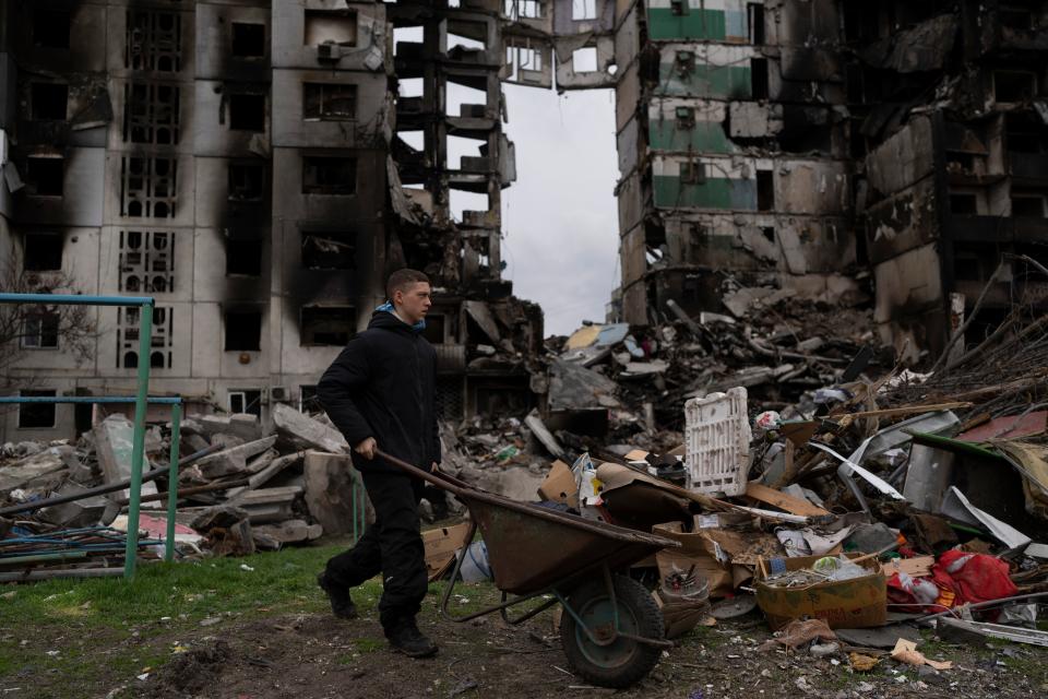 A young man pushes a wheelbarrow in front of a destroyed apartment building in the town of Borodyanka, Ukraine.