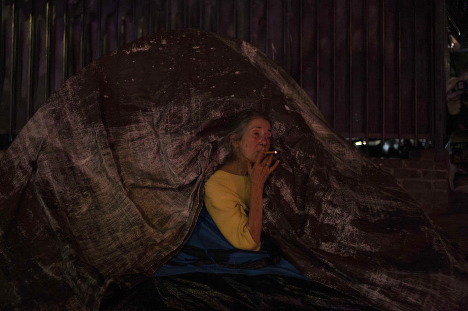 Patricia Sweeney smokes a cigarette through a small gap in her tent as her partner sleeps inside the tent in Los Angeles Tuesday, Oct. 17, 2023. There is no single reason why Los Angeles became a magnet for homelessness. Two contributing factors: Soaring housing prices and rents punish those with marginal incomes, and a long string of court decisions made it difficult for officials to clear encampments or relocate homeless people from parks and other public spaces. (AP Photo/Jae C. Hong)