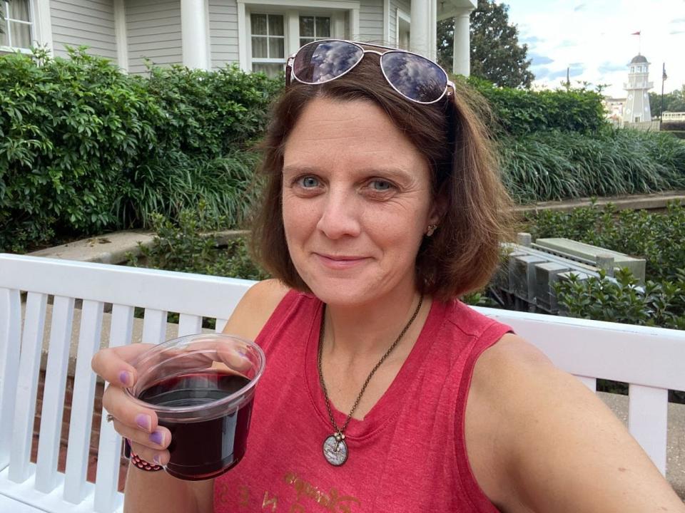 kari holding a cup of wine while sitting on a bench outside of a disney resort