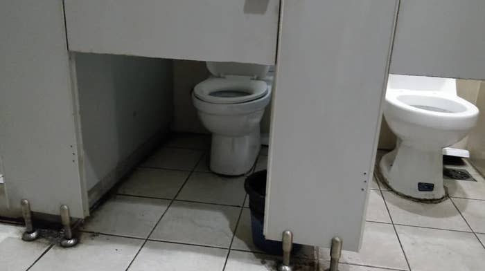 Public restroom with two toilet stalls, but the stall doors don't cover the toilet