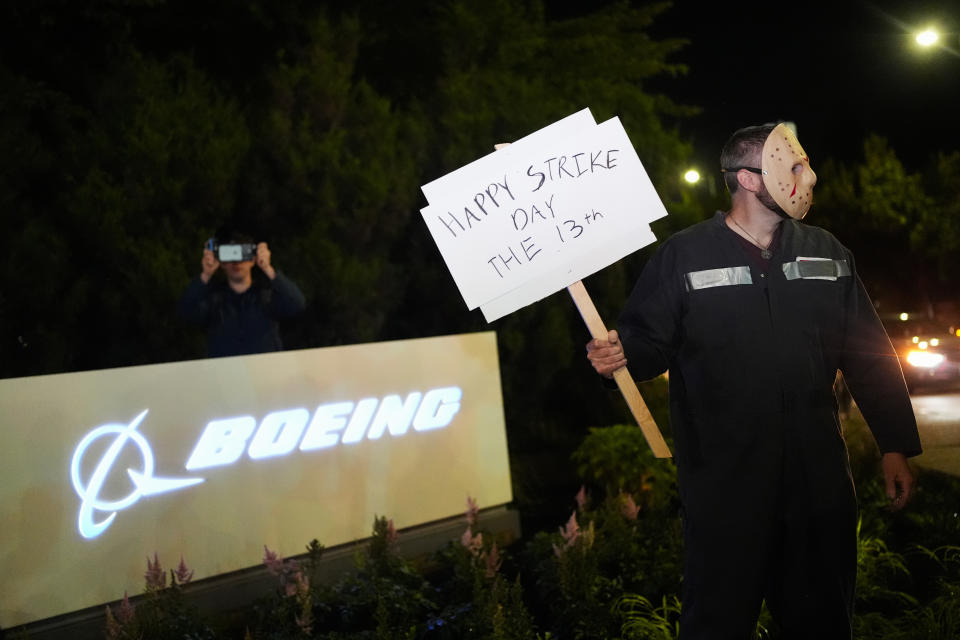 A Boeing worker wears a mask while holding a "happy strike day" sign after union members voted overwhelmingly to reject a contract offer and go on strike Friday, Sept. 13, 2024, outside the company's factory in Renton, Wash. (AP Photo/Lindsey Wasson)