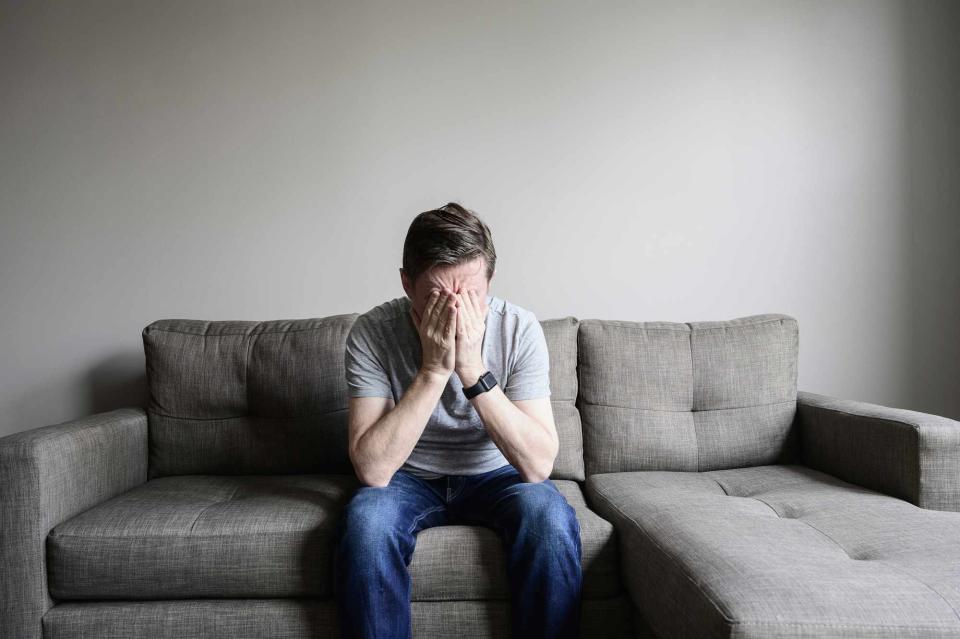 <p>Getty</p> Man on sofa with hands on face.