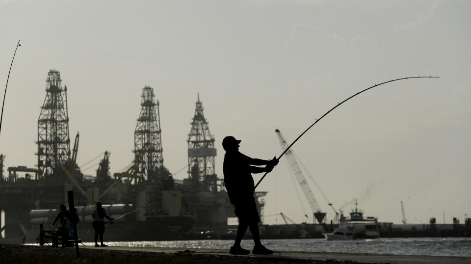 A man fishes near docked oil drilling platforms, Friday, May 8, 2020, in Port Aransas, Texas. Texas' stay-at-home orders due to the COVID-19 pandemic have expired and Texas Gov. Greg Abbott has eased restrictions on many businesses, churches, state parks and beaches. (AP Photo/Eric Gay)