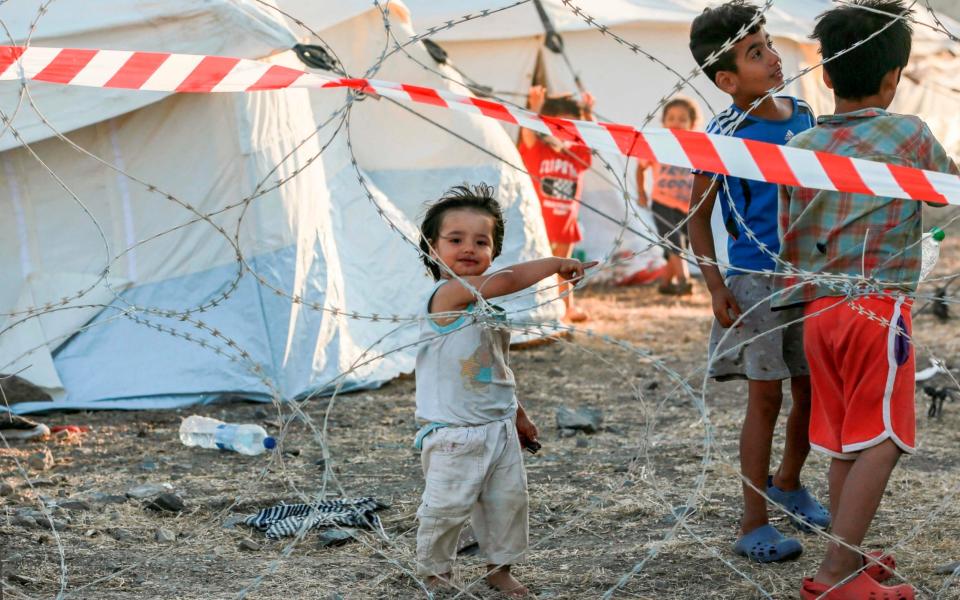 Youngsters of migrant families stand behind barbwire at a quarantine area in the new temporary camp near Mytilene on the Greek island of Lesbos - AFP