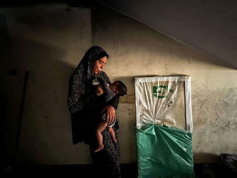 A displaced Palestinian woman helps her son drinks milk at a school classroom where she shelters, amid food scarcity, as Israel-Hamas conflict continues, in Khan Younis