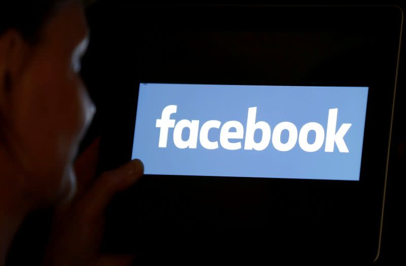 FILE PHOTO: A woman looks at the Facebook logo on a screen.