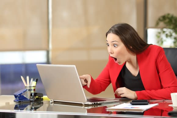 Excited professional woman in a red dress, pointing at her laptop screen in amazement.