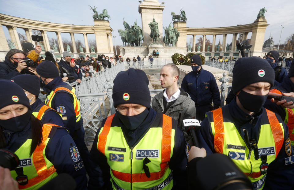 Aron Ecsenyi, center right, the protest organizer, stands behind a police line while his ID is checked in Budapest, Hungary, Sunday, Jan. 31, 2021. Protesters gathered at a central square in Hungary's capital of Budapest on Sunday demanding a rethinking of the country's lockdown restrictions. As the lockdown limiting restaurants to take-away service approaches the three-month mark, many business owners complain that they have received little to none of the government’s promised financial assistance while other businesses like shopping malls and retail stores have been permitted to remain open. (AP Photo/Laszlo Balogh)