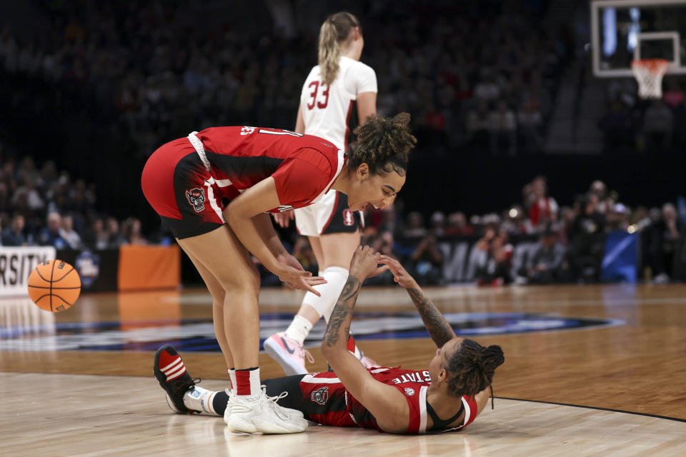 North Carolina State guard Madison Hayes, left, helps up North Carolina State guard Aziaha James during the first half of a Sweet 16 college basketball game against Stanford in the women's NCAA Tournament, Friday, March 29, 2024, in Portland, Ore. (AP Photo/Howard Lao)