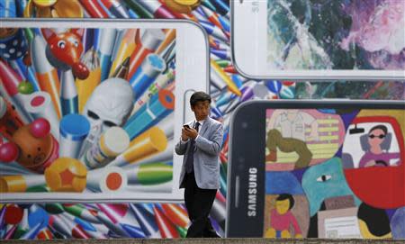 A man uses his mobile phone in front of a giant advertisement promoting Samsung Electronics' new Galaxy S5 smartphone, at an art hall in central Seoul April 15, 2014. REUTERS/Kim Hong-Ji