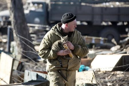 A fighter with the separatist self-proclaimed Donetsk People's Republic army holds a cat as he looks for ammunition in a destroyed Ukrainian army compound in the town of Debaltseve February 22, 2015. REUTERS/Baz Ratner