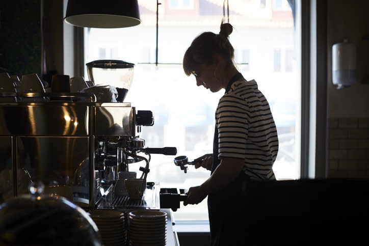 Person with a ponytail and striped shirt making coffee behind a counter in a coffee shop