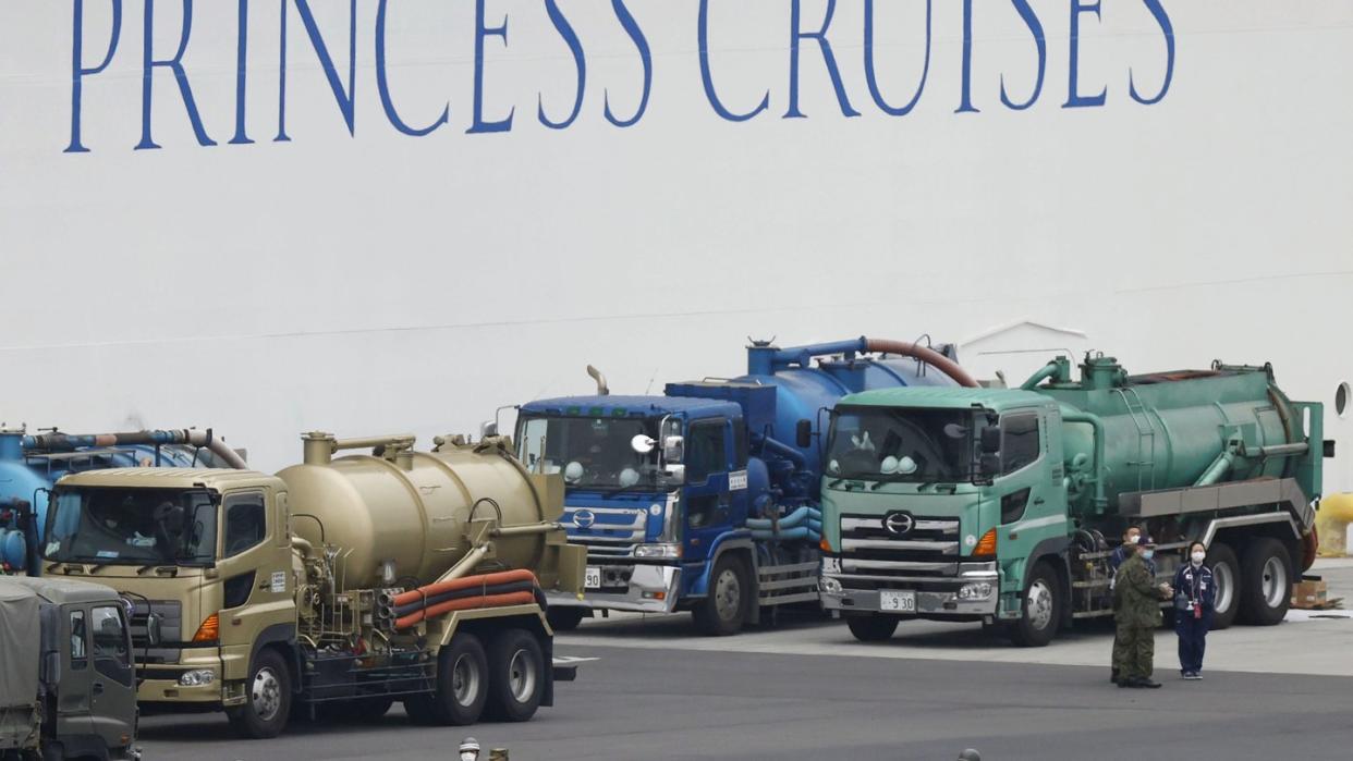 Menschen mit Mundschutz und teilweise mit Schutzanzügen gehen im Hafen von Yokohama an dem unter Quarantäne stehenden Kreuzfahrtschiff «Diamond Princess» vorbei.