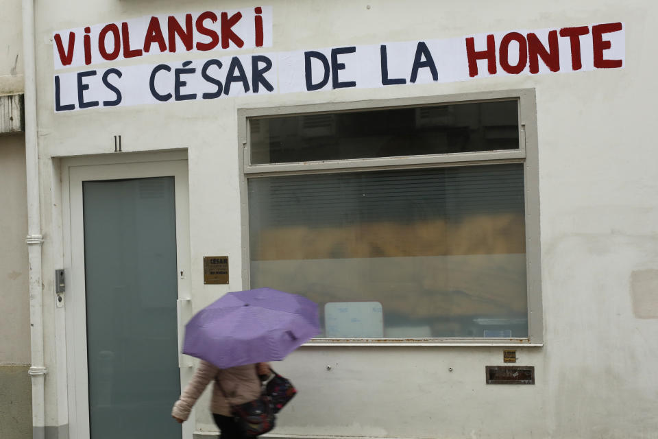 Una mujer pasa frente a la sede de la Academia del César, donde un graffiti dice "Violanski, los César de la vergüenza", en un juego de palabras entre violación y el nombre de Roman Polanski, el jueves 27 de febrero del 2020 en París. Activistas por los derechos de las mujeres protestan las múltiples nominaciones del cineasta al equivalete francés del Oscar luego que una mujer francesa lo acusó de haberla violado en la década de 1970, algo que él niega. (AP Foto/Thibault Camus)