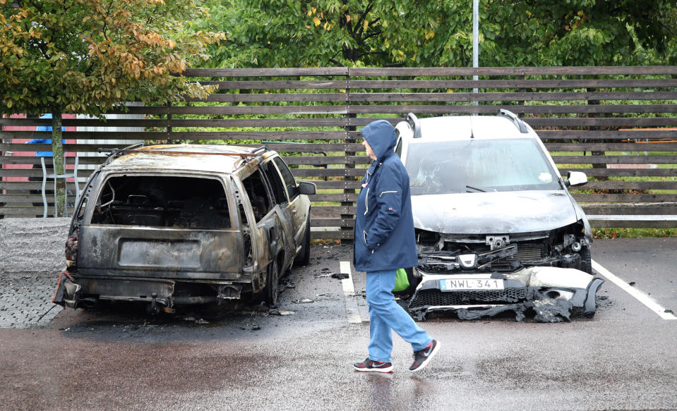 A person walks past burned cars parked at Frolunda Square in Gothenburg, Tuesday, Aug. 14, 2018. Masked youth torched dozens of cars overnight in Sweden and threw rocks at police, prompting an angry response from the prime minister, who on Tuesday spoke of an "extremely organized" night of vandalism. (Adam Ihse/TT via AP)