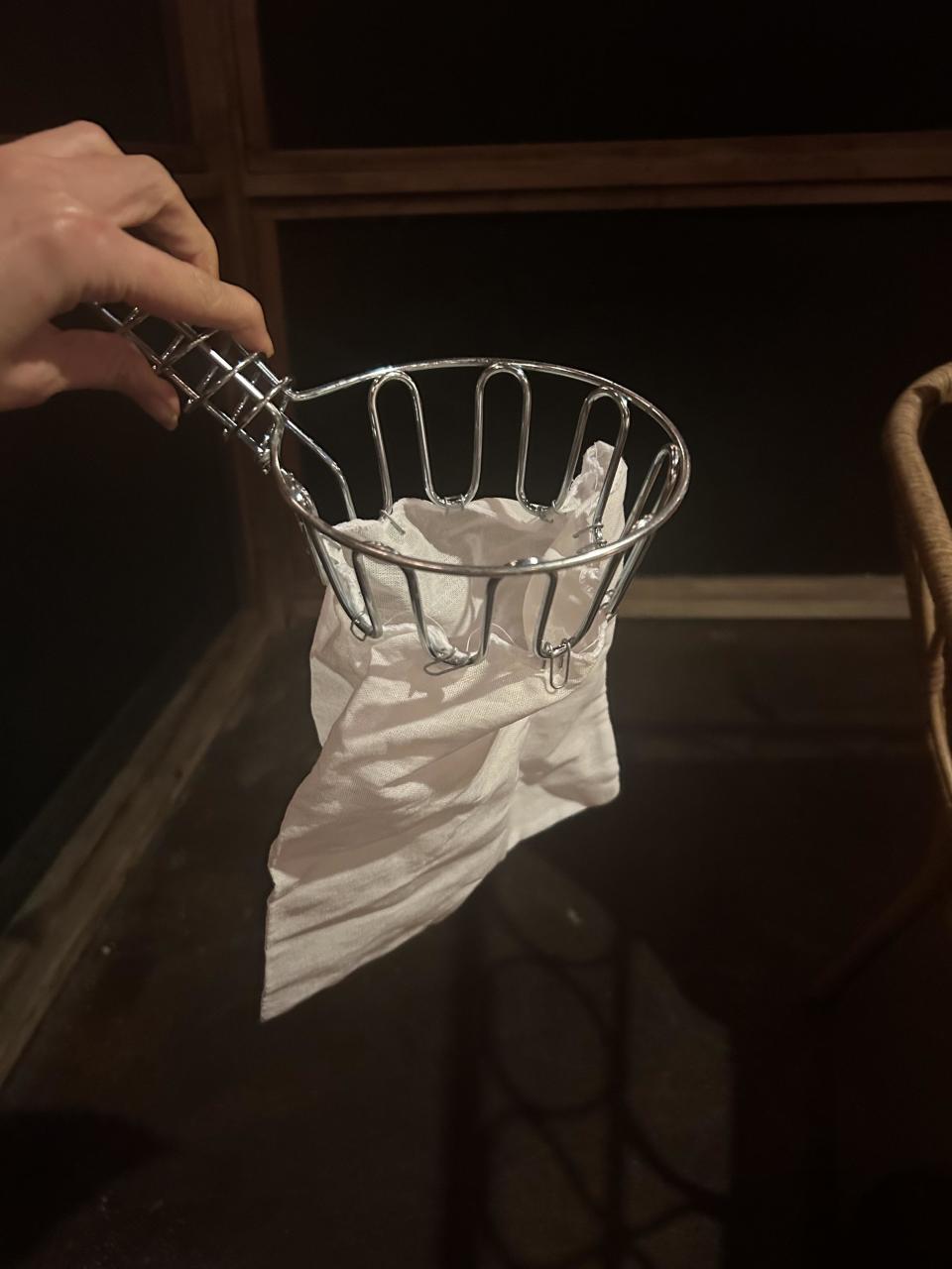 A hand is shown holding a small metal trash can with a napkin inside. There are no people visible in the background