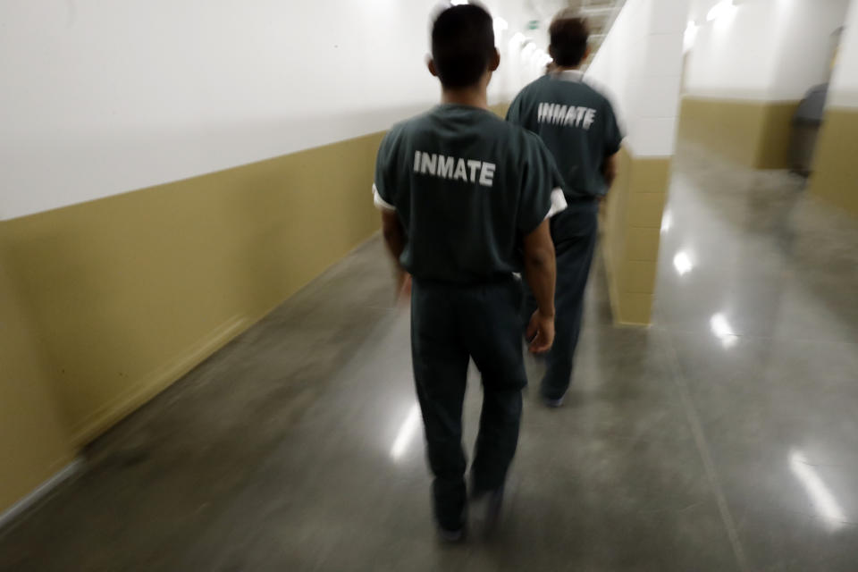 Inmates walk down a hallway at the Otay Mesa Detention Center Wednesday, Aug. 23, 2017, in San Diego. The facility was at the center of the first big novel coronavirus outbreak at a U.S. immigration detention center in April 2020. (AP Photo/Gregory Bull)