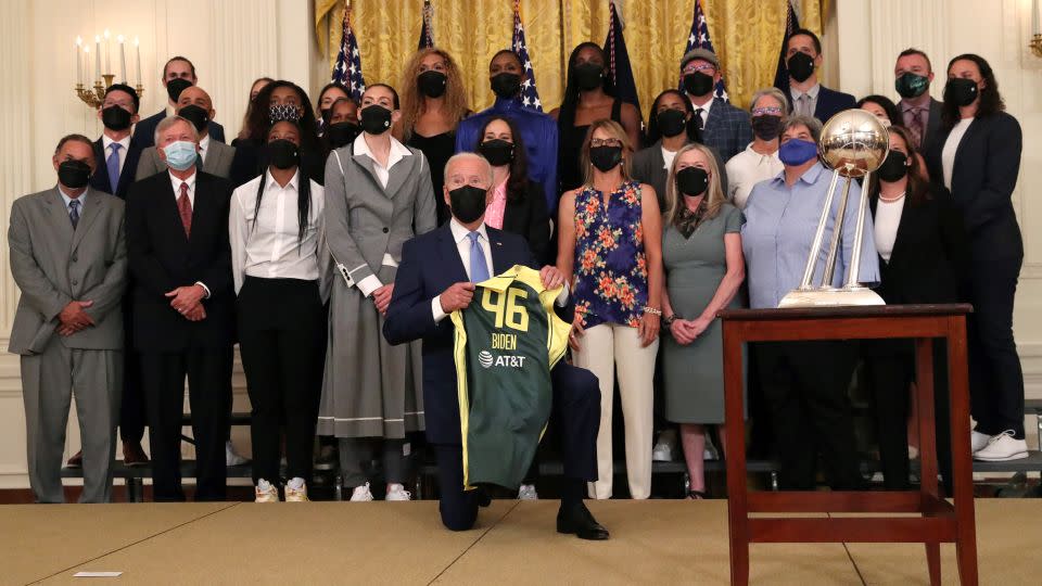 US President Joe Biden holds up a jersey he was gifted as he kneels for a group photograph with members of the Seattle Storm 2020 WNBA Championship women’s basketball team at the White House in Washington, U.S., August 23, 2021. - Leah Millis/Reuters