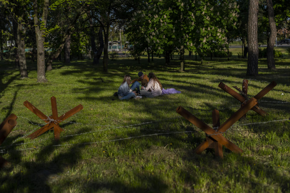 People sit in a park next anti-tank hedgehogs in Kyiv, Saturday, May 6, 2023. (AP Photo/Bernat Armangue)