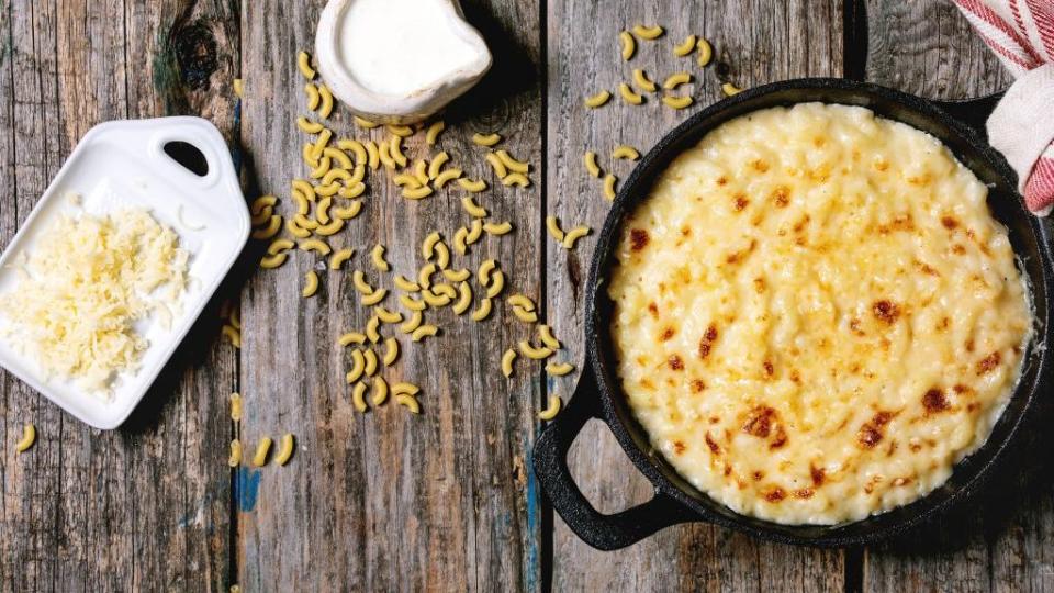 classic american dish baked mac and cheese in cast iron pan with kitchen towel and ingredients above over old wooden background