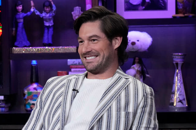 Craig Conover smiling in a striped suit and white, knitted, shirt at WWHL in New York City.