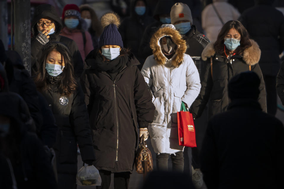 People wearing face masks to protect against the spread of the coronavirus walk along a street during the morning rush hour in Beijing, Wednesday, Dec. 30, 2020. Beijing has urged residents not to leave the city during the Lunar New Year holiday in February, implementing new restrictions and mass testings after several coronavirus infections last week. (AP Photo/Mark Schiefelbein)