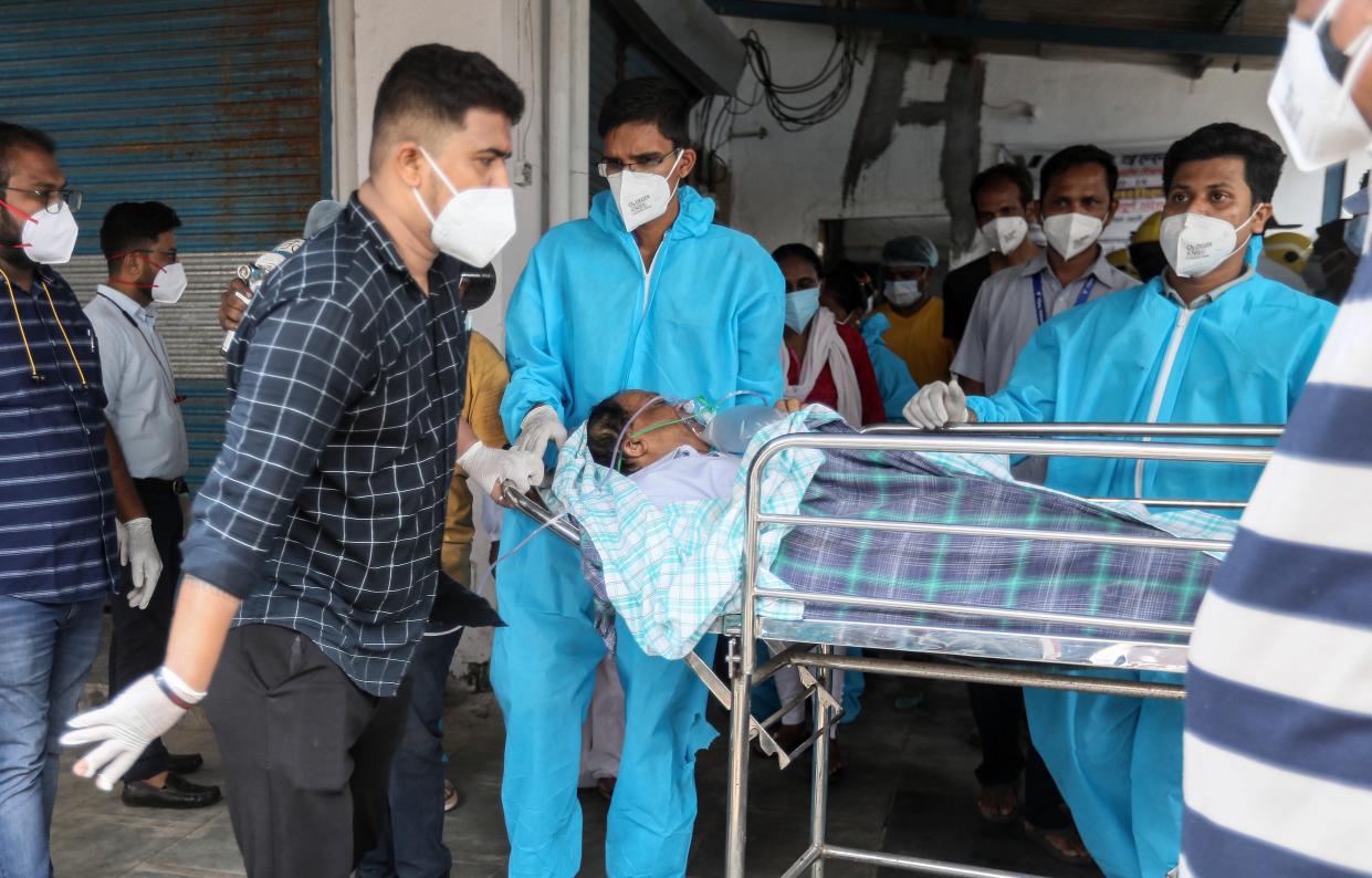 <p>Health workers move a suspected Covid-19 patient outside the Vijay Vallabh hospital in the aftermath of a fire</p> (EPA)