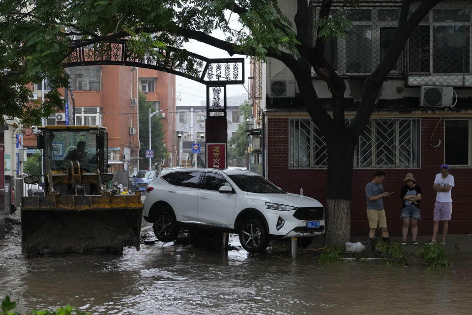 A bulldozer is used to push out mud from a neighbourhood as residents stand near a vehicle left stranded by flood waters in the Mentougou district on the outskirts of Beijing, Tuesday, Aug. 1, 2023. Chinese state media report some have died and others are missing amid flooding in the mountains surrounding the capital Beijing. (AP Photo/Ng Han Guan)