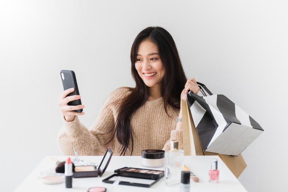 A young woman takes a selfie with purchased cosmetics products.