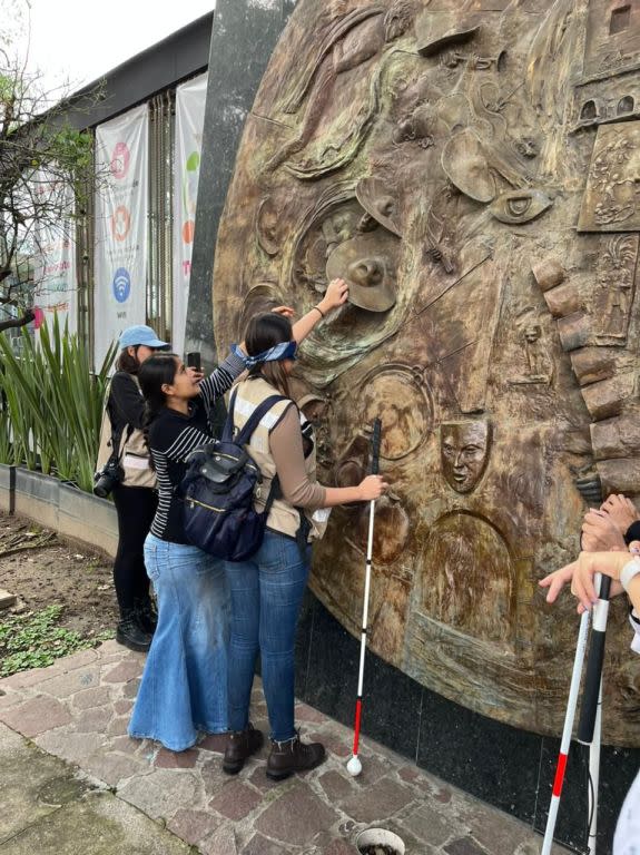 Persona con discapacidad visual tocando un mural de piedra en Tlaquepaque.