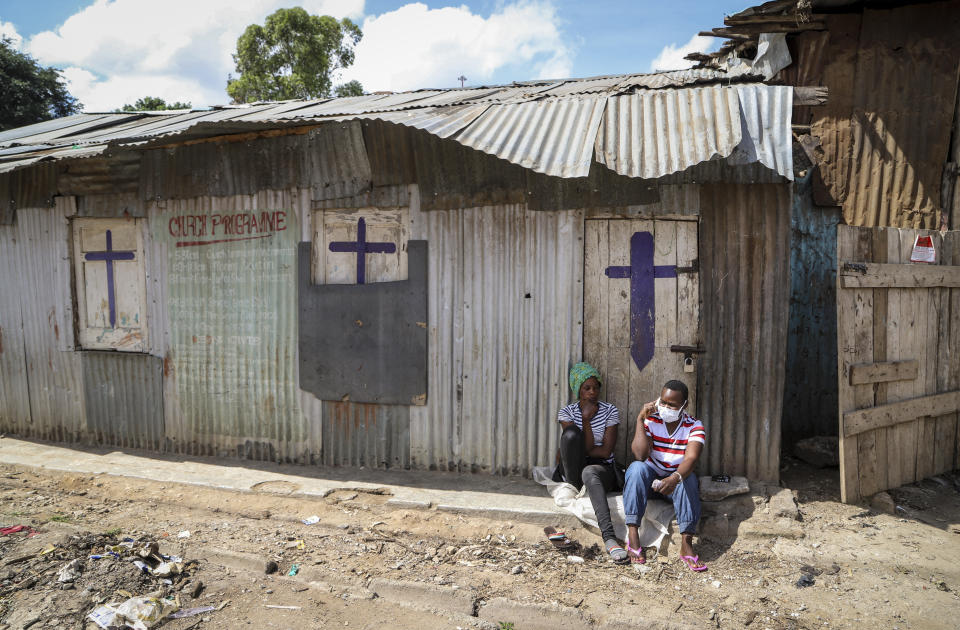 FILE - In this Sunday, April 12, 2020 file photo, two residents sit outside a closed church, after religious public services were stopped to limit the spread of the coronavirus, in the Mathare slum, or informal settlement, of Nairobi, Kenya. The COVID-19 pandemic is testing the patience of some religious leaders across Africa who worry they will lose followers, and funding, as restrictions on gatherings continue. (AP Photo/Patrick Ngugi, File)