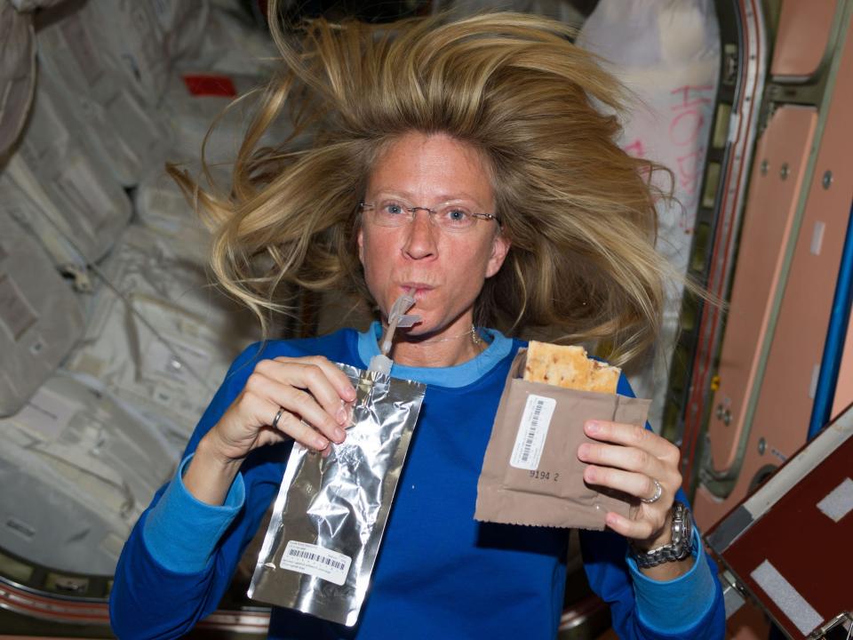 Astronaut Karen Nyberg floating inside space station drinks from pouch with straw while holding a packet with dry food