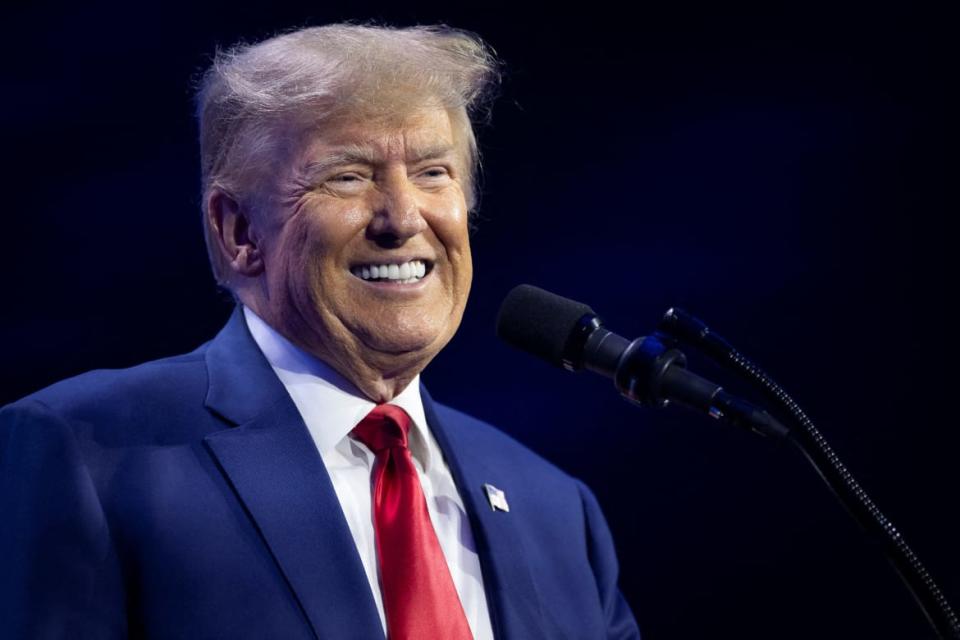 Donald Trump smiles behind a microphone and podium on stage.