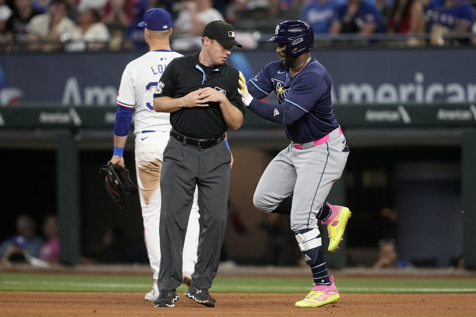 Tampa Bay Rays' Yandy Diaz, right, runs into umpire Junior Valentine, front left, while rounding the bases past Texas Rangers first baseman Nathaniel Lowe, back left, after hitting a three-run home run in the seventh inning of a baseball game in Arlington, Texas, Saturday, July 6, 2024. (AP Photo/Tony Gutierrez)