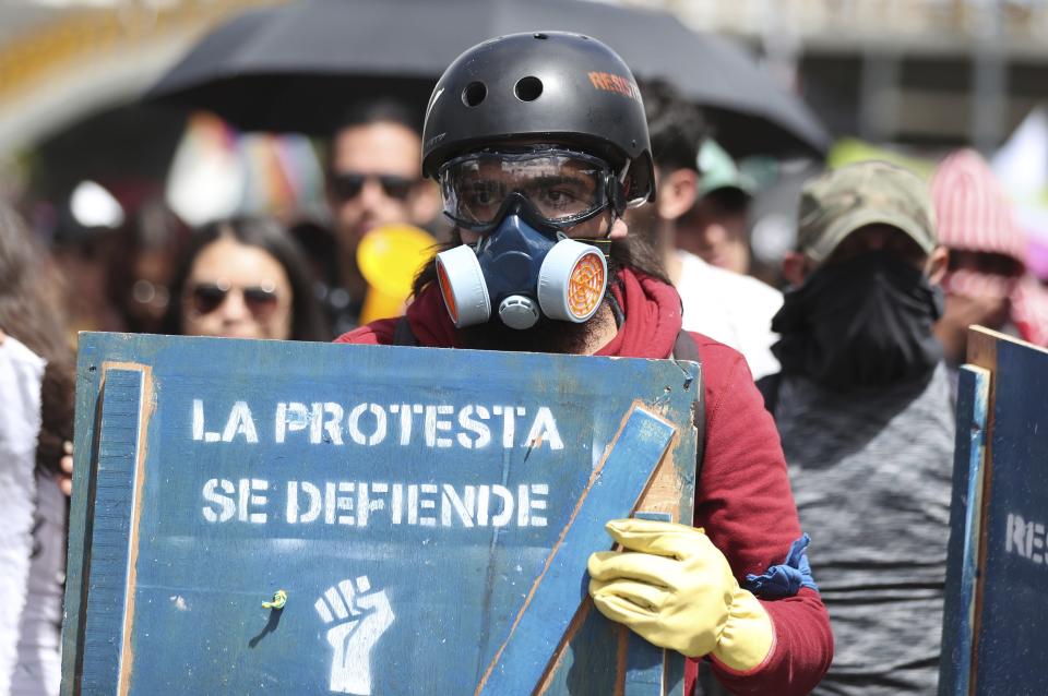 An anti-government demonstrator carries a shield with text stenciled on it that reads "Protests are defended" during a national strike in Bogota, Colombia, Wednesday, Dec. 4, 2019. Colombia’s recent wave of demonstrations began with a massive strike on Nov. 21 that drew an estimated 250,000 people to the streets. Protests have continued in the days since but at a much smaller scale. (AP Photo/Fernando Vergara)