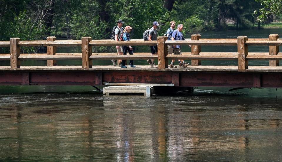 Yosemite National Park visitors cross the bridge which barely clears the water level on the Merced River at the Swinging Bridge picnic area in Yosemite Valley on Tuesday, June 14, 2023.