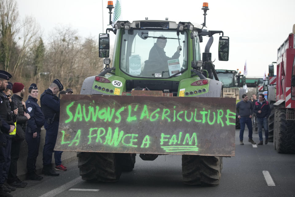 Police forces watch a farmerdriving his tractor with inscription "Save farming, France is hungry" on a highway, Monday, Jan. 29, 2024 in Argenteuil, north of Paris. Protesting farmers were encircling Paris with tractor barricades and drive-slows on Monday, using their lumbering vehicles to block highways leading to France's capital to pressure the government over the future of their industry, which has been shaken by repercussions of the Ukraine war. (AP Photo/Christophe Ena)