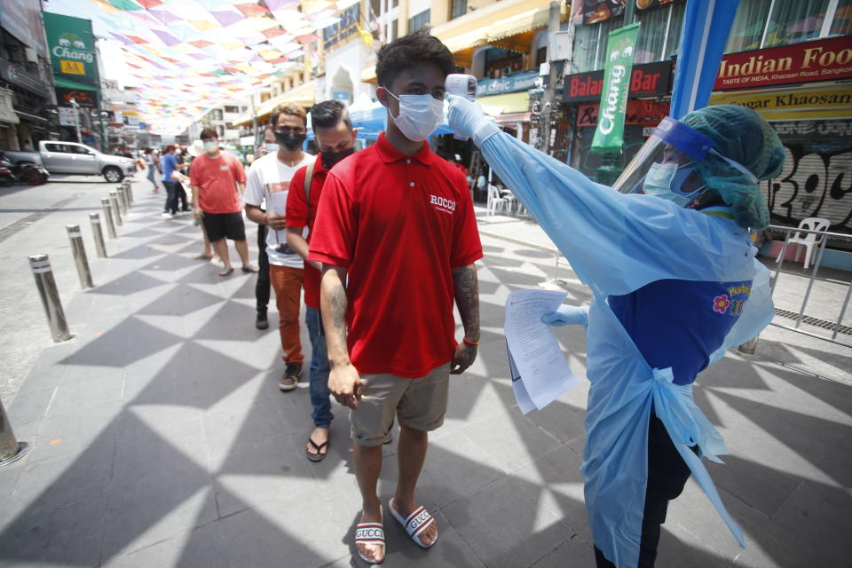 A health worker checks the temperature of a man falling in line for a COVID-19 swab test in Khaosan Road in Bangkok, Thailand Wednesday, April 14, 2021. Thailand recorded more than 1,000 COVID-19 infections on Wednesday, setting a daily record and adding pressure on the government to do more to control the country's spiking transmission rates. (AP Photo/Somchai Chanjirakitti)