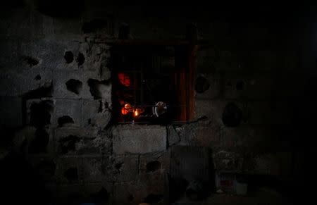 A Palestinian woman is seen from the window of her kitchen as she uses a candle light to prepare food during a power cut in Beit Lahiya town, in the northern Gaza Strip, July 13, 2017. REUTERS/Mohammed Salem