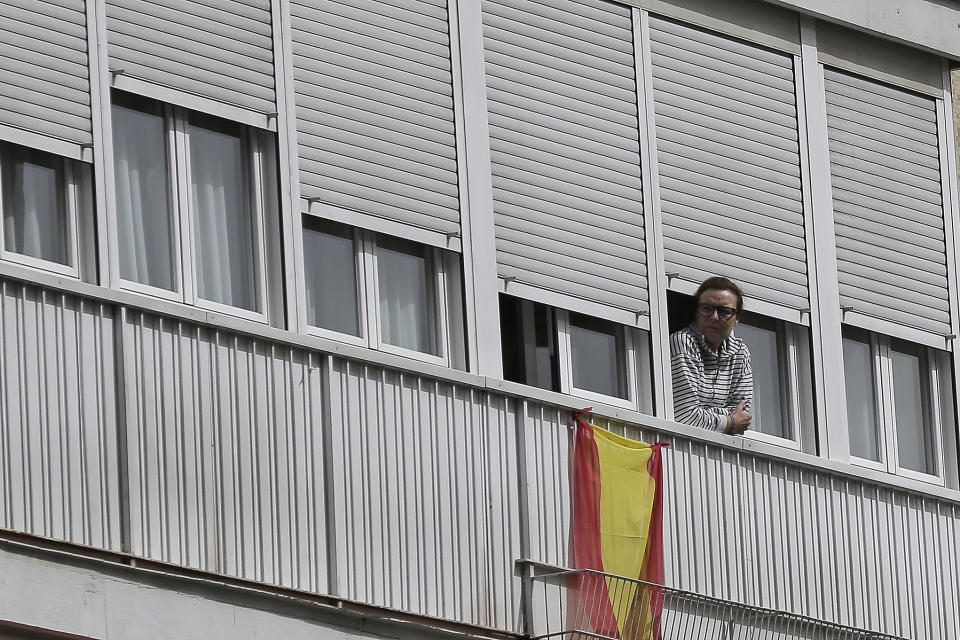 FILE - In this March 19, 2020, file photo, a woman looks out from a balcony next to a Spanish flag in Madrid, Spain. Residents are snitching on businesses and neighbors as authorities worldwide work to enforce business shutdowns and stay-at-home orders meant to limit person-to-person contact amid the coronavirus pandemic. Police in Spain, sometimes aided by videos and photos posted online by zealous citizens, or “balcony police”, have arrested nearly 2,000 people and fined over 230,000 for violating quarantine orders. (AP Photo/Manu Fernandez, File)