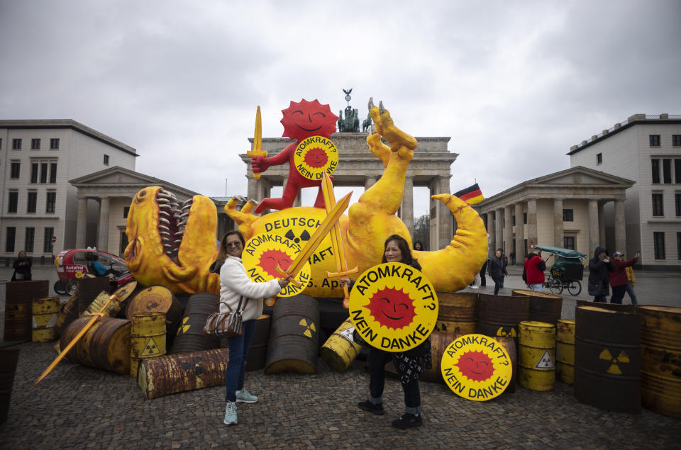 People pose in front of a mock-up dinosaur set-up by Greenpeace in front of the Brandenburg Gate during a rally marking the nuclear shutdown in Germany in Berlin, Germany, Saturday, April 15, 2023. Germany is shutting down its last three nuclear power plants on Saturday, April 15, 2023, as part of an energy transition agreed by successive governments. (AP Photo/Markus Schreiber)