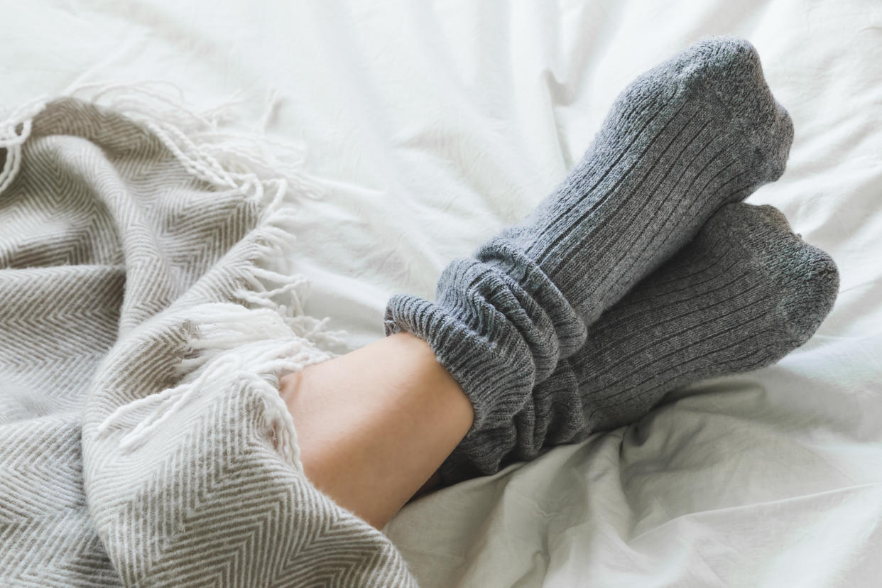Pair of feet in gray socks on a bed under a cozy blanket.