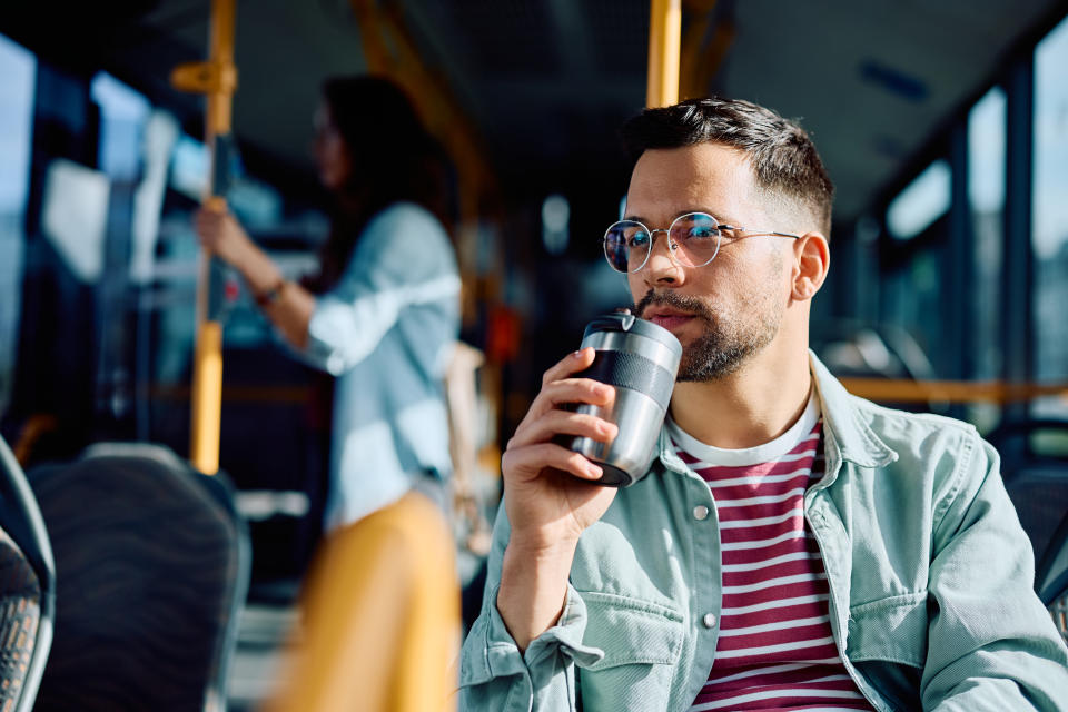 Young man drinking coffee to go while traveling by public transport.