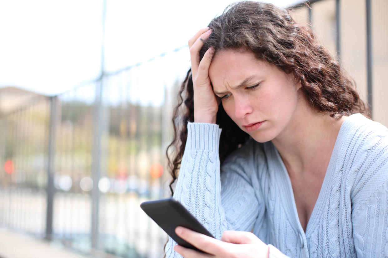 Worried woman checking cell phone in the street