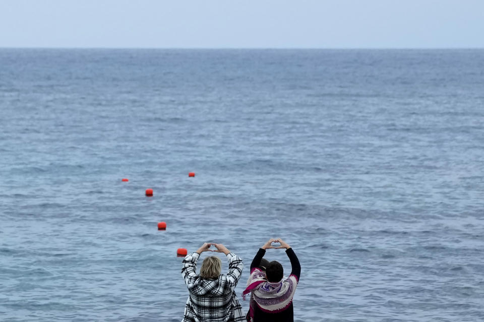 Nadine Kalache Maalouf, right, and Celine Elbacha make heart signs as they face their Lebanese homeland while standing on a deck at the seaside, in the eastern coastal resort of Paralimni, Cyprus, Wednesday, Dec. 22, 2021. They are among the thousands of Lebanese, including teachers, doctors and nurses who have left the country amid a devastating economic crisis that has thrown two thirds of the country’s population into poverty since October 2019. (AP Photo/Petros Karadjias)