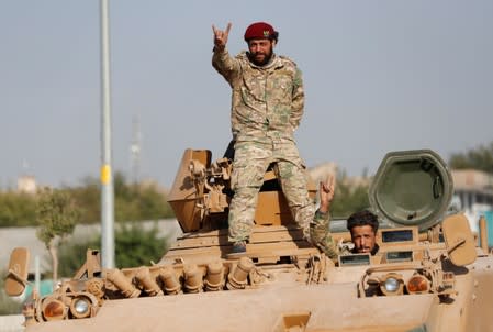 Members of Syrian National Army, known as Free Syrian Army, react as they drive on top of an armored vehicle in the Turkish border town of Ceylanpinar