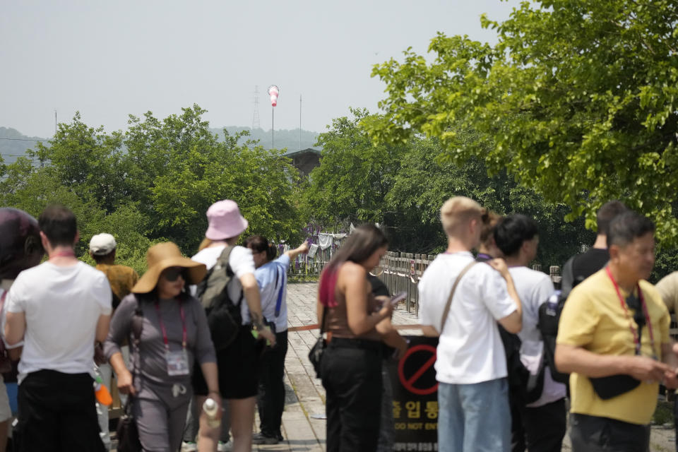 Visitors stand near a wire fence decorated with ribbons written with messages wishing for the reunification of the two Koreas at the Imjingak Pavilion in Paju, South Korea, Tuesday, June 11, 2024. South Korean soldiers fired warning shots after North Korean troops briefly violated the tense border earlier this week, South Korea's military said Tuesday, as the rivals are embroiled in Cold War-style campaigns like balloon launches and propaganda broadcasts.(AP Photo/Lee Jin-man)